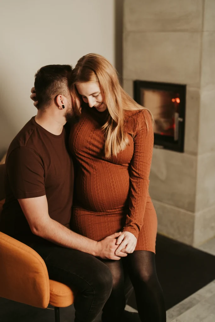Recenze „Těhotenské focení – Lucie“ – přirozený intimní portrét páru v interiéru u krbu v teplém světle.