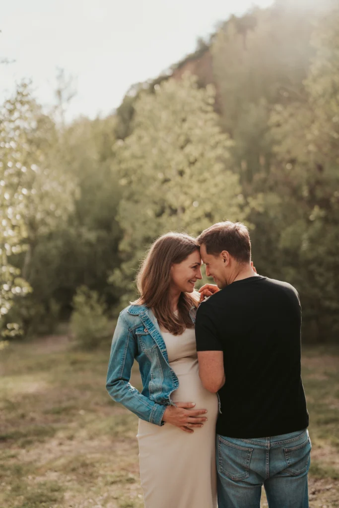 Recenze – těhotenské focení: přirozený moment páru v přírodě, partneré se obejmou a drží bříško v jemném večerním světle.