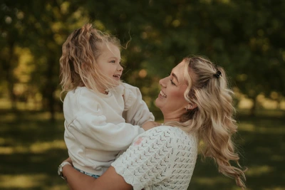 Maminka zvedá malou holčičku do náruče při focení venku