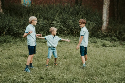 Tři bratři se drží za ruce při společné hře na louce