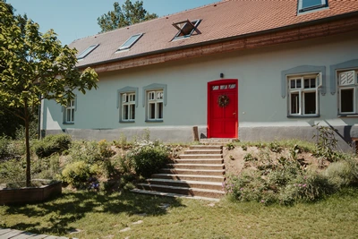 Bílý venkovský dům s červenými dveřmi a zahradou
