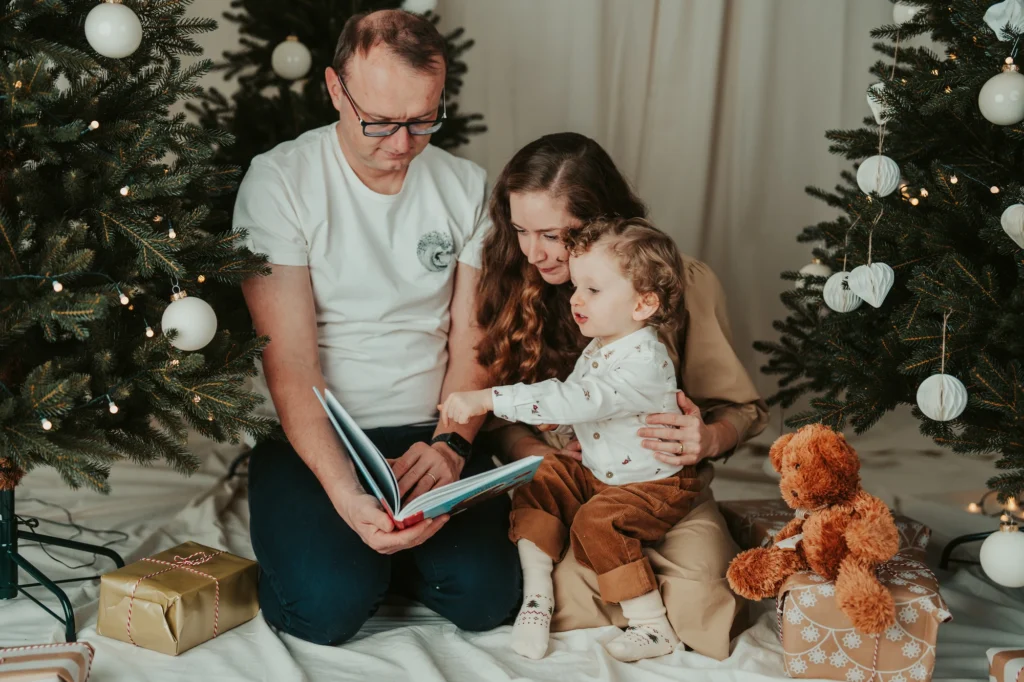 Alena, Michal a Noe si společně prohlížejí otevřenou knížku u stromku.