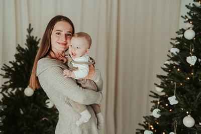 Maminka drží miminko mezi vánočními stromky